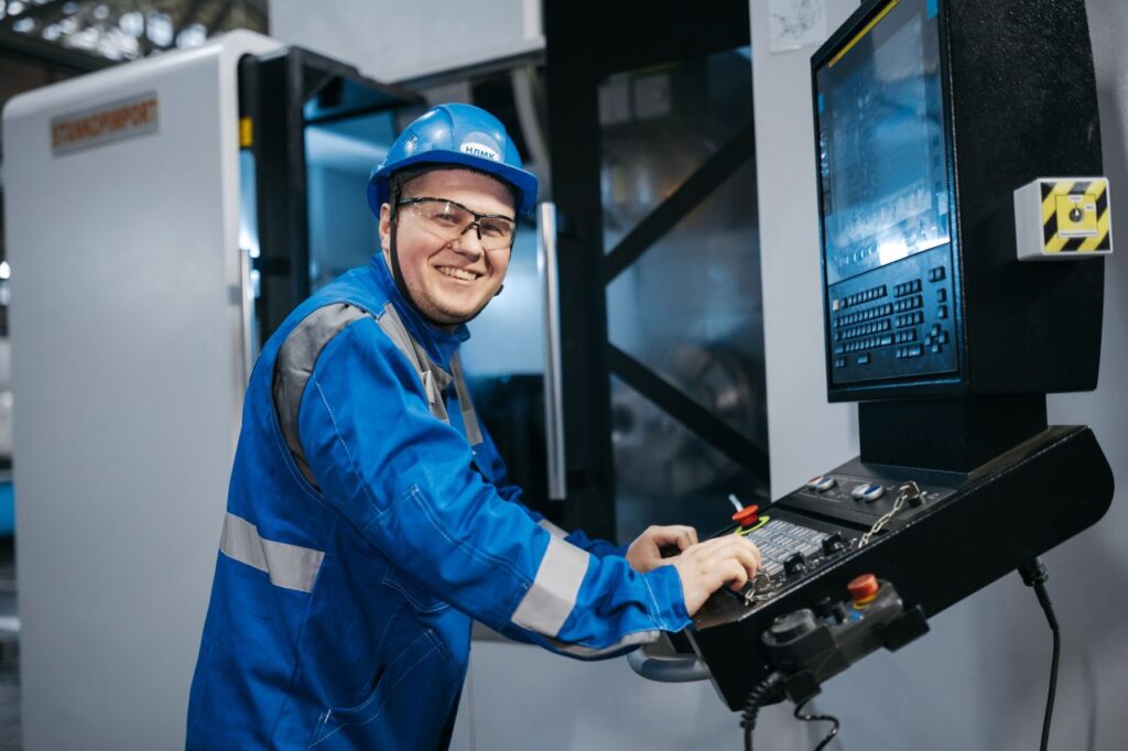 Smiling worker in blue uniform and hard hat using CNC machine indoors in Russia.